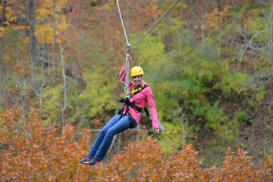 A woman ziplining at camp kern in the fall